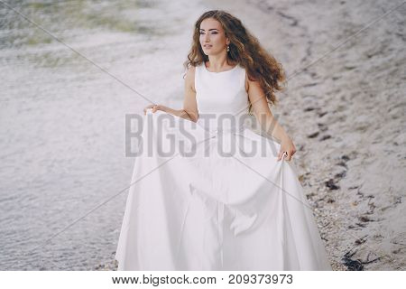 Beautiful long-haired bride in a magnificent white dress walking on a beach