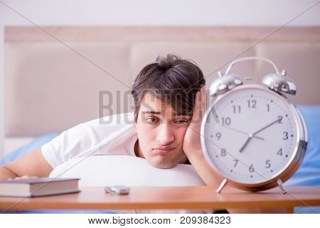 Man in bed frustrated suffering from insomnia with an alarm cloc