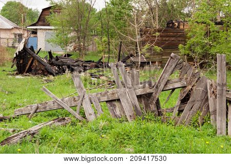 a broken fence behind which are the remains of a burned wooden house