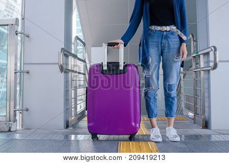 Close up legs of the young woman standing at the airport with a suitcase