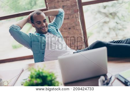 Cheerful Black Guy Is Watching At His Laptop Screen, At His Work Place, With Arms Behind The Head, R