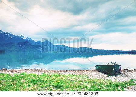Abandoned Fishing Paddle Boat On Bank Of Alps Lake. Morning Lake Glowing By Sunlight.