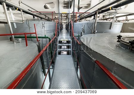 Narrow and long staircase between large tanks. Large steel cylindrical tanks for fermenting the yeast mixture. Shop fermentation distillery.