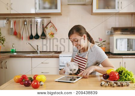 A Young Pretty Woman With White Persian Cat In The Kitchen With Tablet On The Table. Vegetable Salad