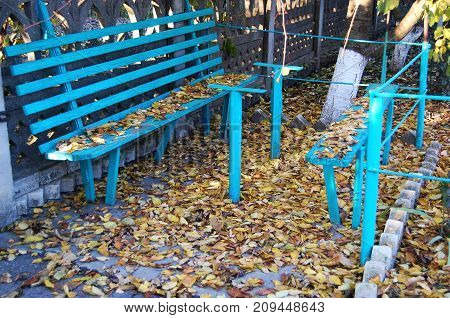 Old blue wooden bench and fallen autumn leaves at a rural dooryard