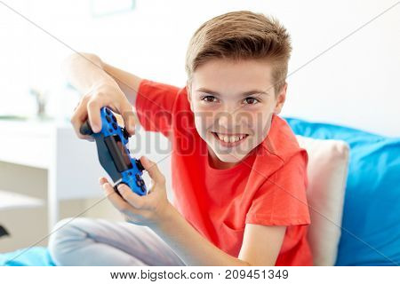 gaming, technology and people concept - smiling boy with gamepad playing video game at home