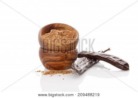 Organic carob pod and carob powder in wooden bowl isolated on white background. Healthy cocoa alternative.