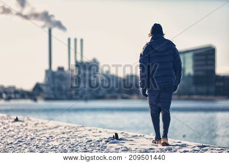 Winter city smog pollution people walking in warm outerwear in cold morning commute. Man runner in down jacket and sportswear shorts walking on snowy street.