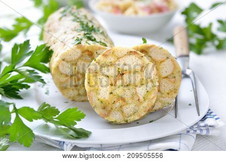 Sliced Bavarian bread dumpling ,  the perfect side dish for roasts  or strips of meat with sauce,  in the background sauerkraut with bacon
