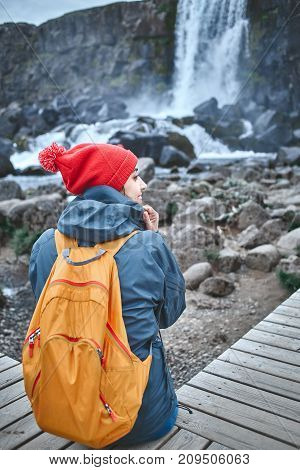 young woman hiker walking in beautiful mountains in Thingvellir valley, Iceland. woman looks at the Oxararfoss waterfall.