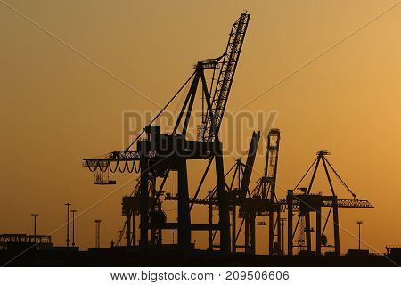 Cranes and shipyard of Hamburg port. Silhouettes of shipyard cranes against the background of the sunset sky in orange tones.