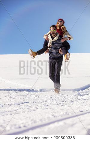 Loving couple playing together in snow outdoor. Winter holidays in mountains. Man and woman wearing knitted clothing having fun on weekends
