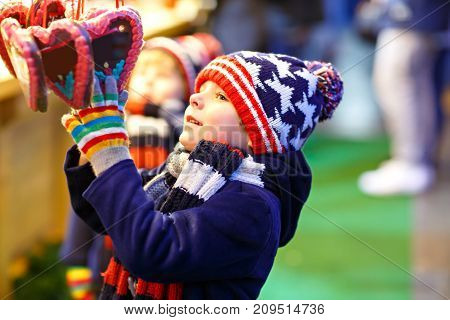 Little cute kid boy buying sweets from a cancy stand on Christmas market. Happy child on traditional family market in Germany. Preschooler in colorful winter clothes.