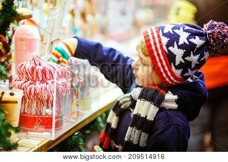 Little cute kid boy buying sweets from a cancy stand on Christmas market. Happy child on traditional family market in Germany. Preschooler in colorful winter clothes.