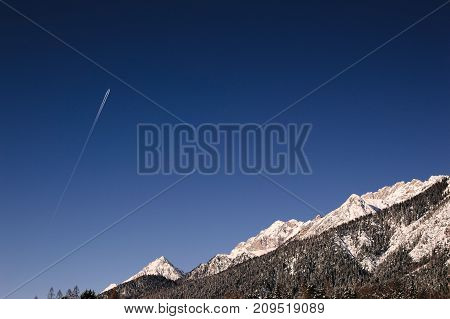 Sky and mountain with passing airplane over it.