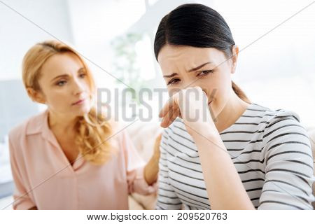 Negative emotions. Cheerless unhappy sad woman turning away from her friend and wiping her nose while crying