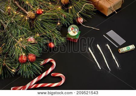 Cocaine divided into paths with Xmas toys and spruce branch on black background top view. Copy space. Still life. Flat lay. New year