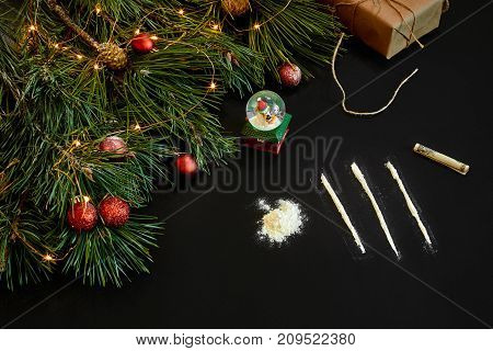 Cocaine divided into paths with Xmas toys and spruce branch on black background top view. Copy space. Still life. Flat lay. New year