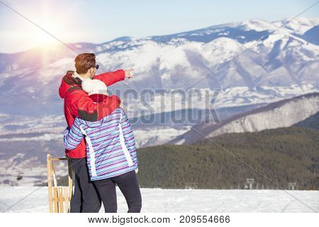 Rear view of a loving couple in fur hood jackets looking at snowed mountain range.