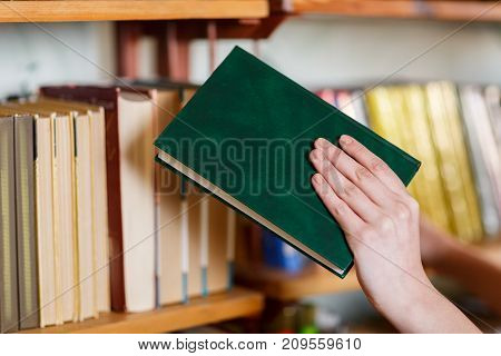 A woman's hand chooses a book in the library. Close-up . The concept of education.