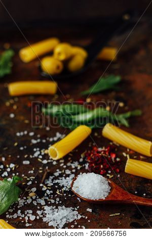 Sea salt in wooden spoon surronded by pasta and other ingredients