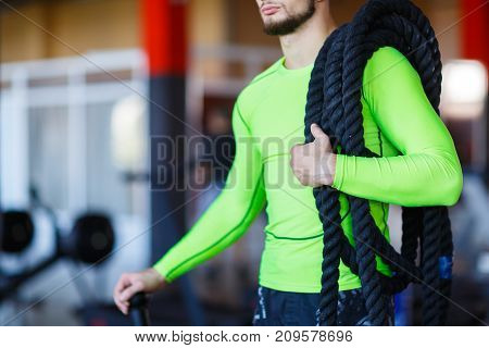 A man with heavy ropes on his shoulders. Photo of a young man in sports clothes with a rope on his shoulders. Strength and motivation.