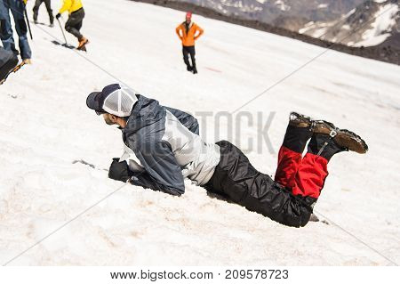 Training to correct slip on a slope or a glacier with the help of an ice ax. A fully equipped backpacker slides on the belly along a snowy slope in the mountains, hindering the glide by an ice ax. Training an inexperienced climber before climbing a mounta