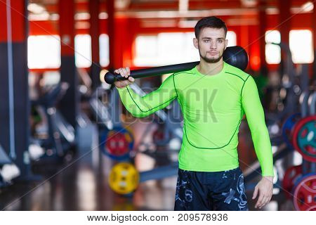 A young man in green posing in the gym with a hammer. Front view. The concept of sport. Healthy lifestyle.