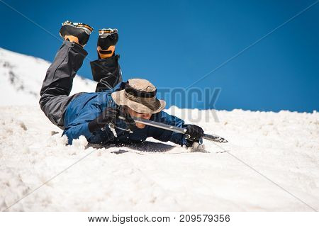 Training to correct slip on a slope or a glacier with the help of an ice ax. A fully equipped backpacker slides on the belly along a snowy slope in the mountains, hindering the glide by an ice ax. Training an inexperienced climber before climbing a mounta