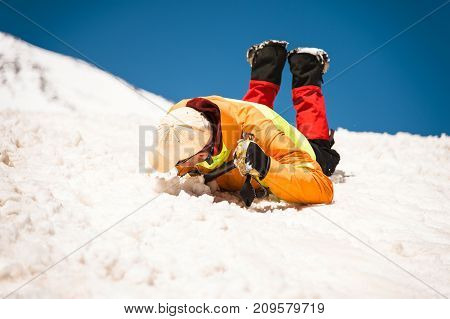 Training to correct slip on a slope or a glacier with the help of an ice ax. A fully equipped backpacker slides on the belly along a snowy slope in the mountains, hindering the glide by an ice ax. Training an inexperienced climber before climbing a mounta