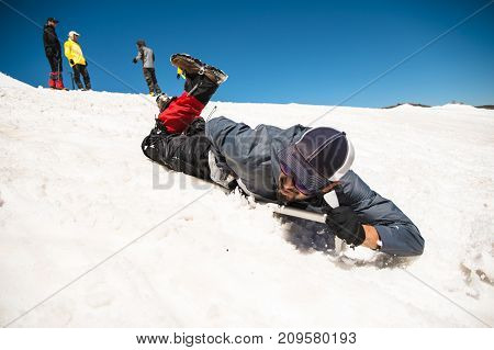 Training to correct slip on a slope or a glacier with the help of an ice ax. A fully equipped backpacker slides on the belly along a snowy slope in the mountains, hindering the glide by an ice ax. Training an inexperienced climber before climbing a mounta