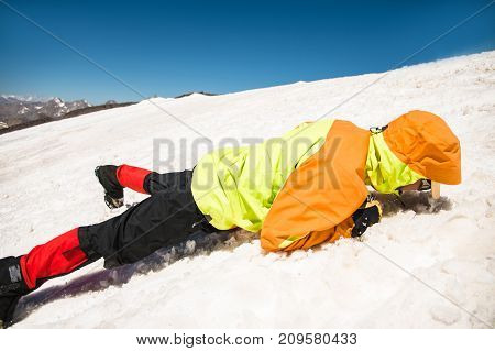 Training to correct slip on a slope or a glacier with the help of an ice ax. A fully equipped backpacker slides on the belly along a snowy slope in the mountains, hindering the glide by an ice ax. Training an inexperienced climber before climbing a mounta
