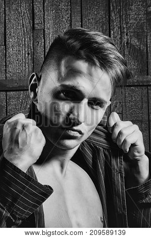 Sexy serious sensual muscular young macho man with bare torso and wet hair in shirt standing indoor on wooden background vertical picture