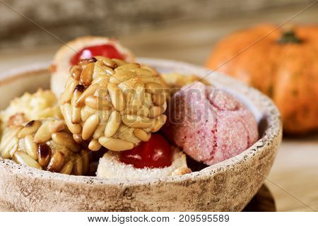 closeup of a rustic bowl with some panellets, typical confection eaten in All Saints Day in Catalonia, Spain, on a wooden table and a pumpkin in the background