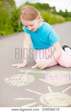 Sunny and warm summer days and happy chilhood. Cute little girl drawing with chalk crayons outdoors.