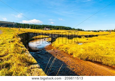 Jizerka stream on green meadow with old small stone bridge, Jizerka village, Jizera Mountains, Czech Republic.