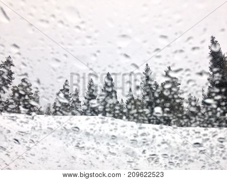 An abstract shot of snow melted droplets on glass looking into a winter wonderland scene.