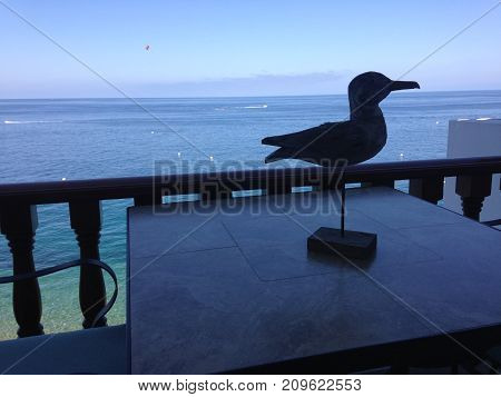 Silhouette of a sandpiper statue rests on the balcony of a ocean front house.