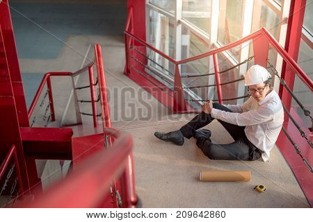 Engineer or Architect feeling tired and frustrated with his job. sitting on building stairs with architectural drawing on his side while wearing protective equipment safety helmet at construction site