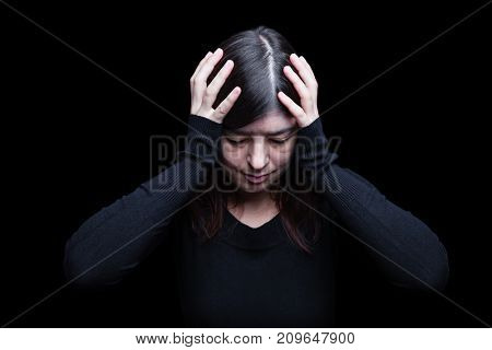 Distressed, woman holding the head with the hands, on a black or dark background. Concept for migraine, headache, pain, depression, despair, suffer, worried, frustration.