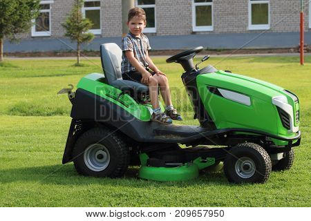 Little boy sits on lawn on green grass near building at summer day