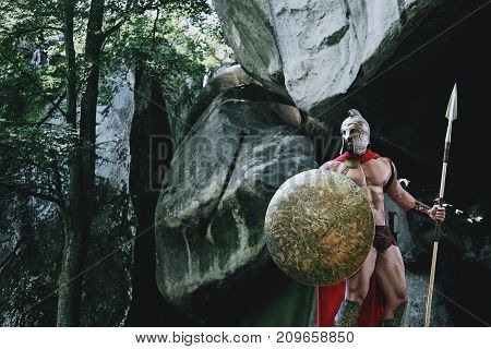 Brave Spartan warrior wandering in the woods walking with his weapon holding a spear and a shield.