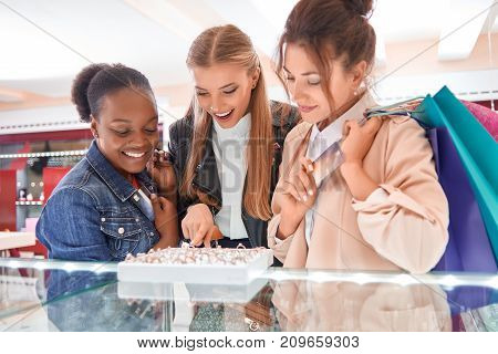 Two cheerful young women helping their best friend choosing a ring at the jewelry store.