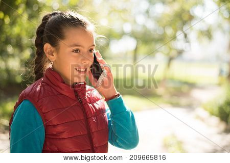 Beautiful girl talking on a smartphone in a red vest on the outdoor.Handsome smiling girl with mobile phone walking on outdoor. Young caucasian girl receiving good news by phone. Portrait smiles girl