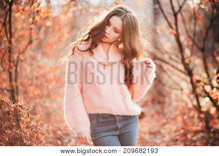 Young sexy thoughtful woman with long hair in fluffy sweater, in orange autumn forest.