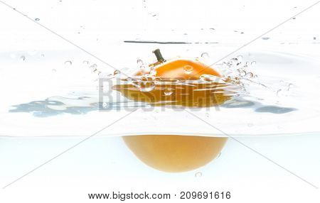 Whole, yellow and ripe tomato falls into the water. Water splashes. Isolated picture on white background