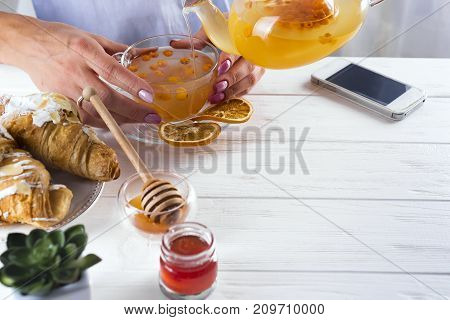 famele hands holding hot cup of sea-buckthorn tea.breakfast with croissants and honey