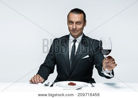 Portrait of a young man in image of maniak with knife, fork and and a piece of raw meat on a plate. Man in suit. The image in the style of Halloween