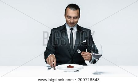Portrait of a young man in image of maniak with knife, fork and and a piece of raw meat on a plate. Man in suit. The image in the style of Halloween
