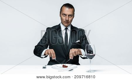 Portrait of a young man in image of maniak with knife, fork and and a piece of raw meat on a plate. Man in suit. The image in the style of Halloween